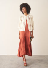 Woman wearing dark orange satin tiered floaty summer dress against a plain background