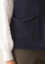 Woman wearing a dark navy blue sleeveless chunky knit waistcoat with green trousers and a white shirt