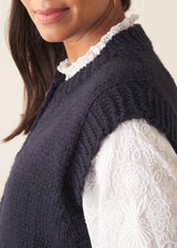 Woman wearing a dark navy blue sleeveless chunky knit waistcoat with green trousers and a white shirt