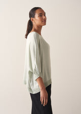 Woman wearing a pale green satin blouse top with black trousers