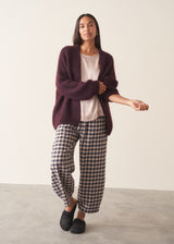 Woman wearing pearlescent light lilac satin top with navy check trousers and a dark plum chunky cardigan