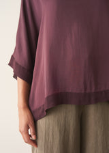 A woman wearing a plum satin top with khaki green trousers