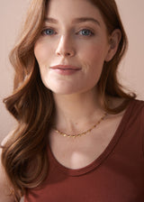Close-up of a woman wearing a gold necklace with heart-shaped charms, styled with a brown jersey vest.