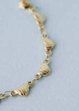 Close-up of a gold necklace with heart-shaped charms, on a blue background