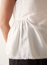 A woman wearing a sleeveless white top with a relaxed, slightly sheer texture and a peplum-like hem, paired with dark wide-leg trousers.