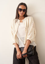 A woman wearing a sleeveless white top with a relaxed, slightly sheer texture and a peplum-like hem, paired with dark wide-leg trousers.