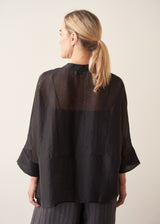 Woman wearing semi-sheer button up black shirt with dark grey wide leg trousers.