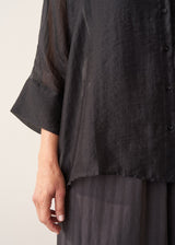 Woman wearing semi-sheer button up black shirt with dark grey wide leg trousers.