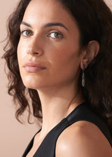 Woman wearing a pair of sparkly silver crystal adorned tear drop earrings, styled with a black waistcoat