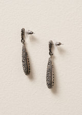 Side view of sparkly silver crystal adorned tear drop earrings on a beige background