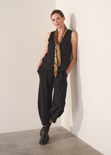Woman wearing black waistcoat and gold sequin scarf against a plain background.