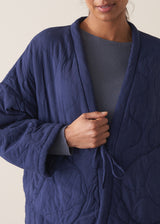 Person wearing a navy blue jacket and white barrel leg trousers against a plain background