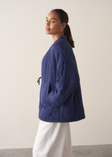 Person wearing a navy blue jacket and white barrel leg trousers against a plain background