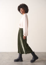 Woman wearing green velvet cropped wide-leg trousers and a pink shirt against a plain background