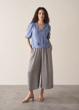 Woman wearing blue textured blouse with tassels and grey stripe trousers
