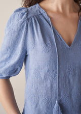 Woman wearing blue textured blouse with tassels and grey stripe trousers