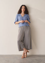 Woman wearing blue textured blouse with tassels and grey stripe trousers