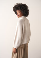 Back of woman wearing a white rollneck sweater and beige wide leg trousers against a white background