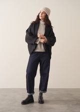 Woman wearing a black quilted kimono jacket over a beige sweater and dark jeans against a plain background