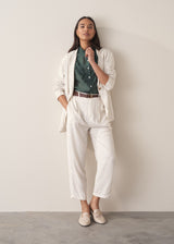 Woman wearing a dark green blouse with ruffled details and cream suit trousers.