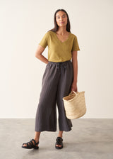 A woman wearing a olive green v-neck t-shirt with grey charcoal stripe trousers and sandals