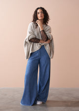 Woman wearing a beige sweater with visible lace sleeves and blue jeans against a beige background