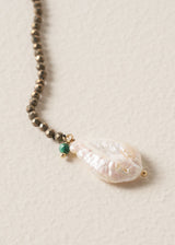 Close up of freshwater pearl detail on a black beaded drop necklace, on a beige backgroun