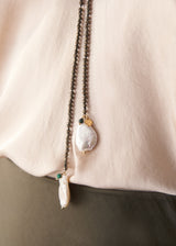Close up of freshwater pearl detail on a black beaded drop necklace, on model wearing satin shirt and skirt