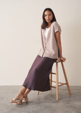 Woman wearing burgundy satin slip skirt with white t-shirt and stone knittted waistcoat