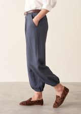 A woman wearing dark blue balloon leg trousers with pleat details and a white cotton shirt.