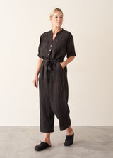 Woman wearing a short sleeve black linen jumpsuit with a button up front and waist tie