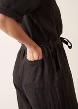 Woman wearing a short sleeve black linen jumpsuit with a button up front and waist tie