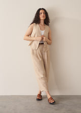 Woman wearing a pair of striped ankle length barrel leg trousers with a striped waistcoat, against a beige background