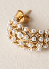 Close up of gold drop stud earrings with a delicate white beads on beige background