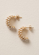 Pair of gold drop stud earrings with a delicate white beads on beige background