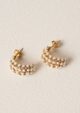 Pair of gold drop stud earrings with a delicate white beads on beige background