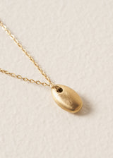 Gold minimal necklace with a simple oval pendant on a beige background