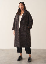 A women wearing a long dark brown leopard print coat with black trousers and a white blouse.