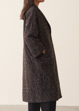 A women wearing a long dark brown leopard print coat with black trousers and a white blouse.