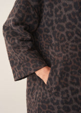 A women wearing a long dark brown leopard print coat with black trousers and a white blouse.