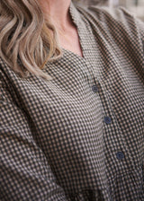 Close-up of a person wearing a brown and beige gingham button-front top, with part of the neck, hair, and torso visible.