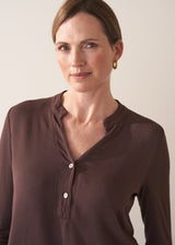 Woman wearing a brown long-sleeve jersey top against a plain background