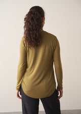 Woman wearing an olive green long-sleeve top with jeans against a plain background