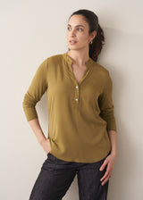 Woman wearing am olive green long-sleeve top with jeans against a plain background
