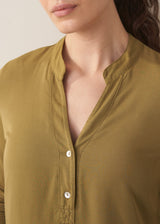 Woman wearing an olive green long-sleeve top against a plain background