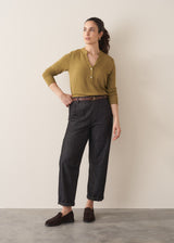 Woman wearing an olive green long-sleeve top with jeans and brown loafers against a plain background