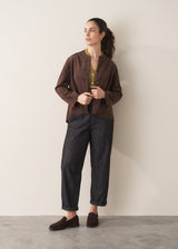 Woman wearing an olive green long-sleeve top with jeans, faux suede jacket and brown loafers against a plain background