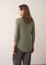Woman wearing a moss green long-sleeve jersey top against a plain background