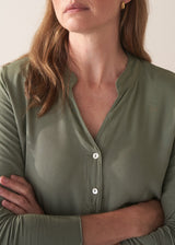 Woman wearing a moss green long-sleeve jersey top against a plain background