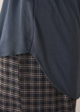 Woman wearing dark grey blue long sleeve jersey top against a plain background